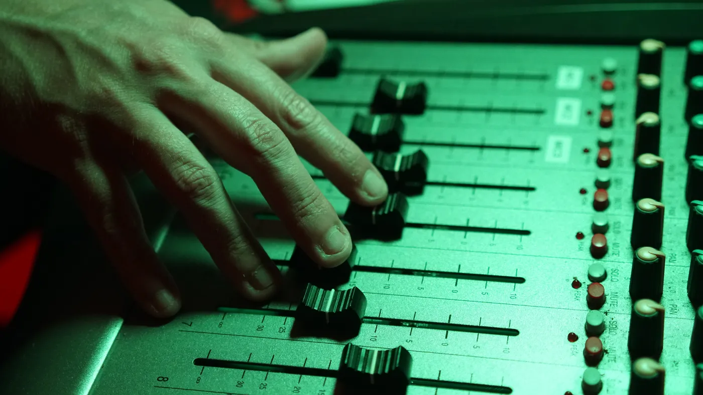 Mano moviendo los faders de la mesa con luz verde